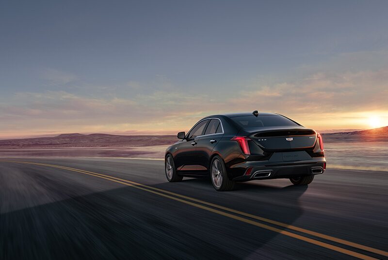 Three Quarters Rear View of a Black Cadillac Driving Down the Road on a Golden Hour Before Evening