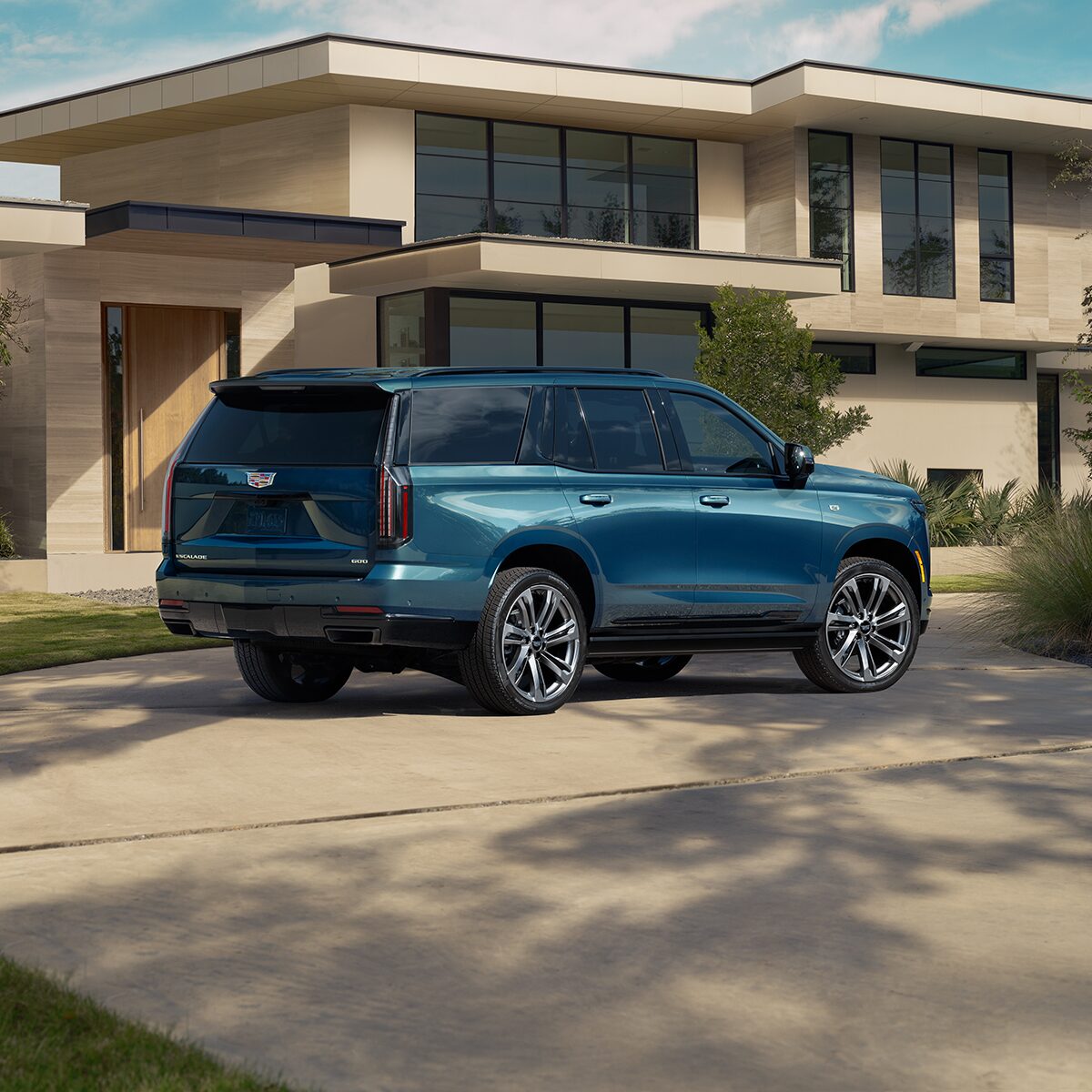Three-Quarter Rear View of a Blue 2026 Cadillac Escalade Parked in Front of a Modern Home