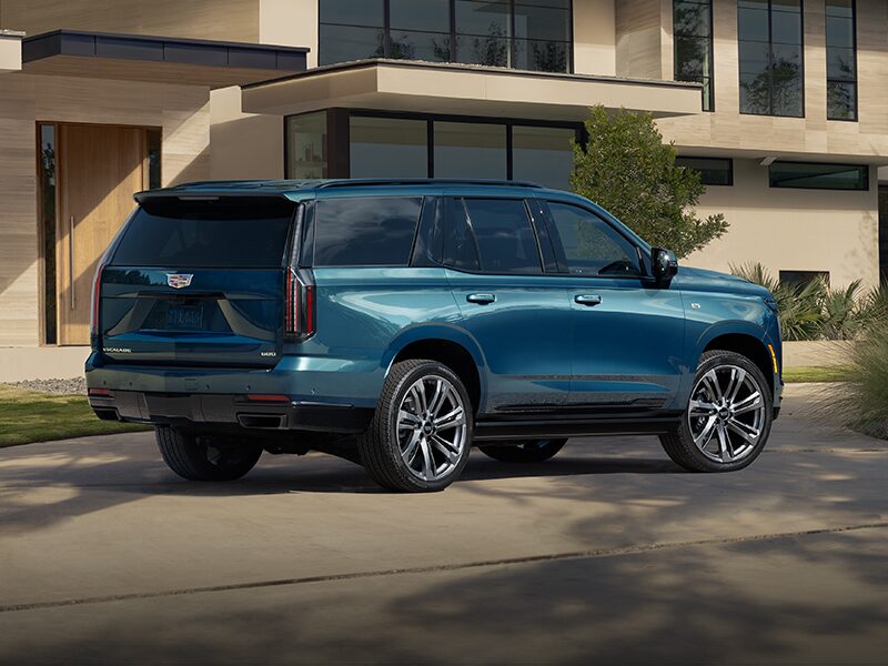 Three-Quarter Rear View of a Blue 2026 Cadillac Escalade Parked in Front of a Modern Home